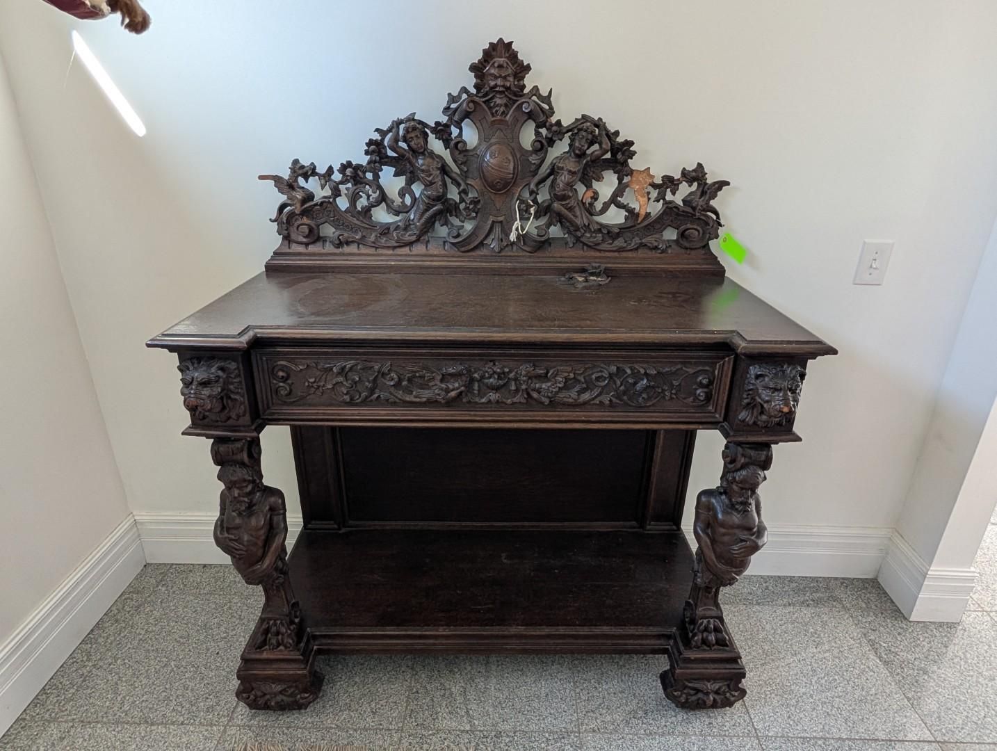 Ornate dark wood antique table with carved details against a white wall.