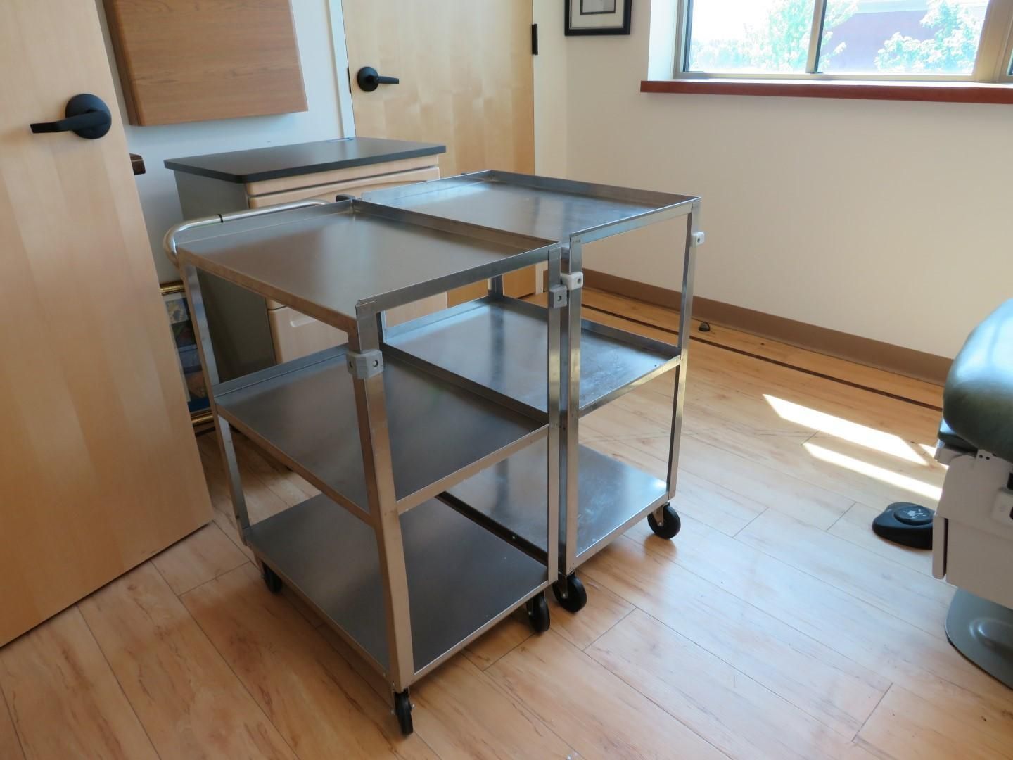 Stainless steel medical cart with multiple shelves, in a medical exam room.