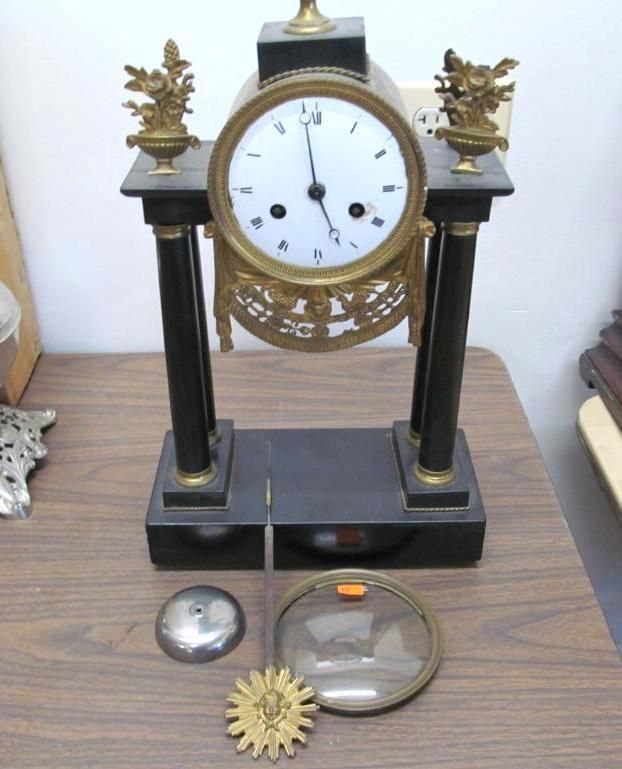 Antique clock on a wooden table. Black base with gold accents, white clock face.
