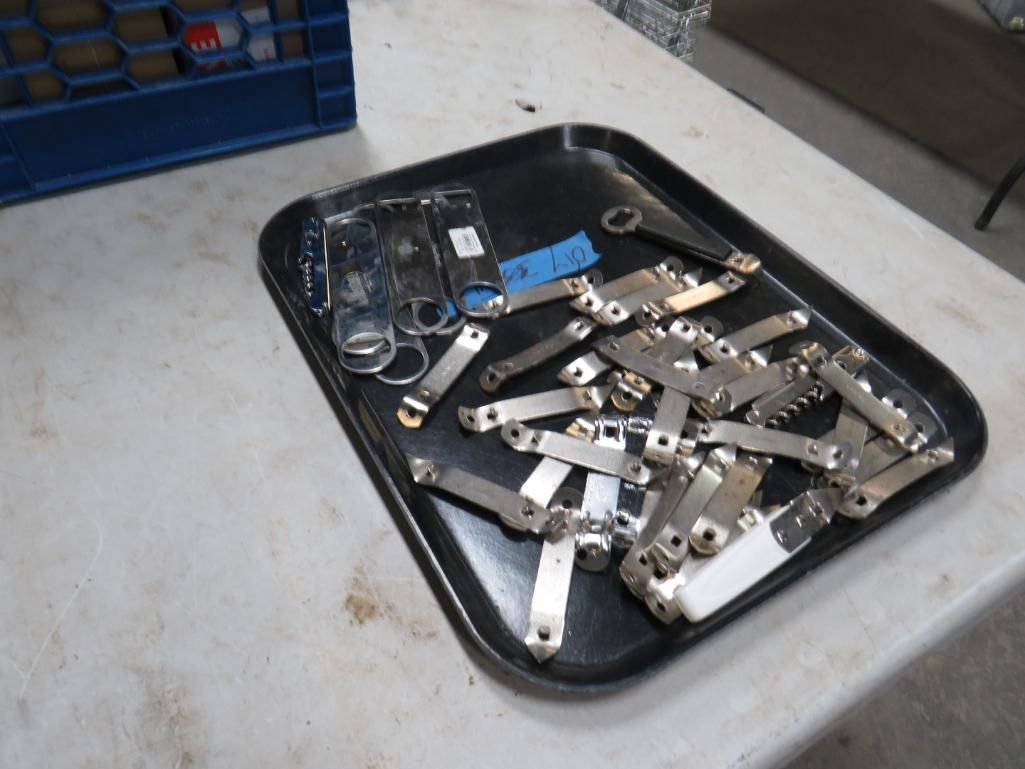 Black tray holding a pile of metal can or bottle openers.
