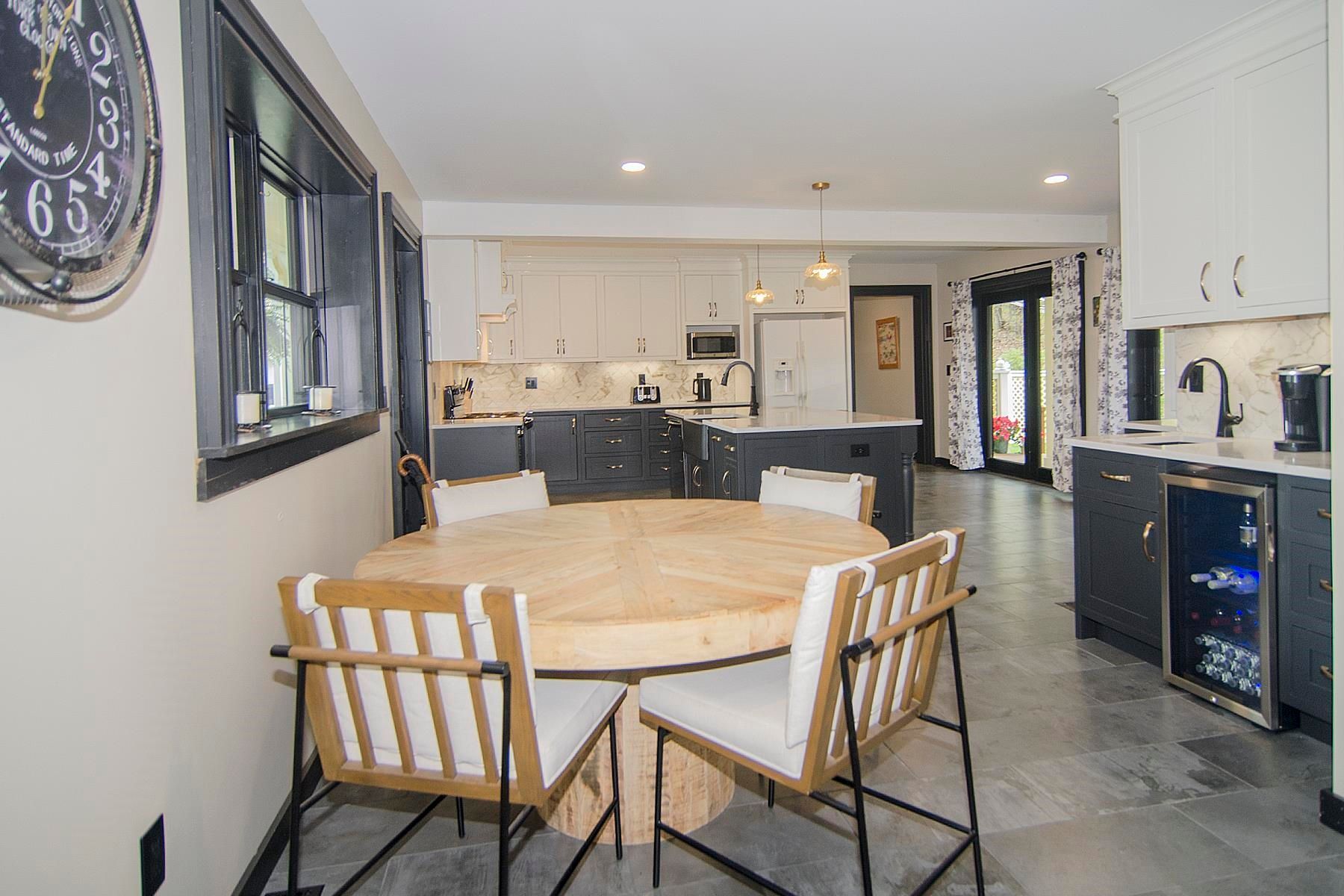 Modern kitchen with round wooden table, chairs, and dark grey cabinets, leading to outdoor space.