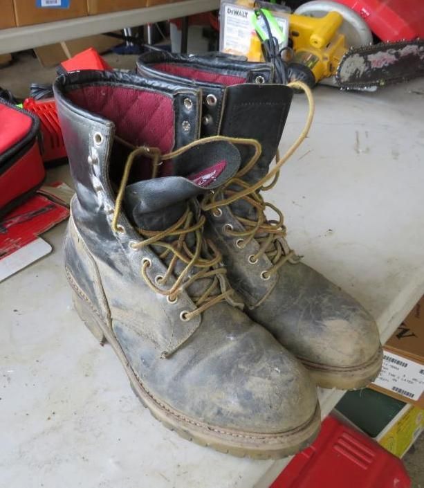 Pair of work boots with tan laces, on a table. Black and gray leather, red lining.