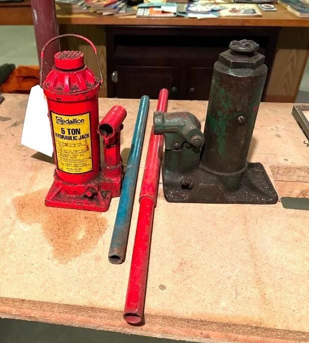 Two car jacks with handles on a wooden surface. One red, one green.