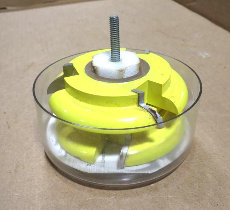 Yellow wooden object with bolt inside a clear cylinder on a surface.