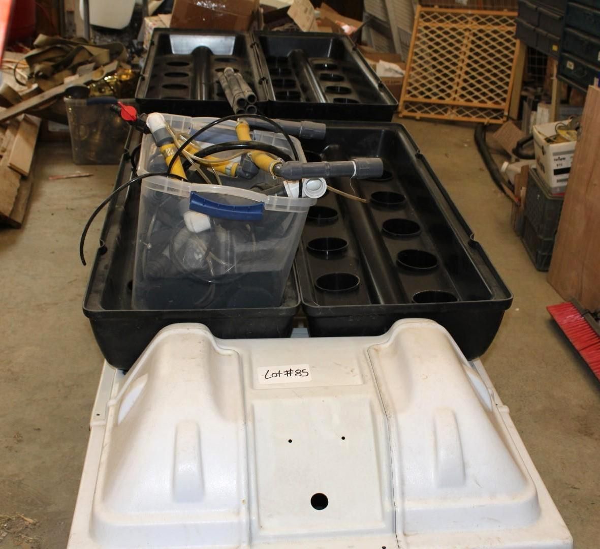 Hydroponic system components, black trays with plant holes, white reservoir, tools in a workshop.