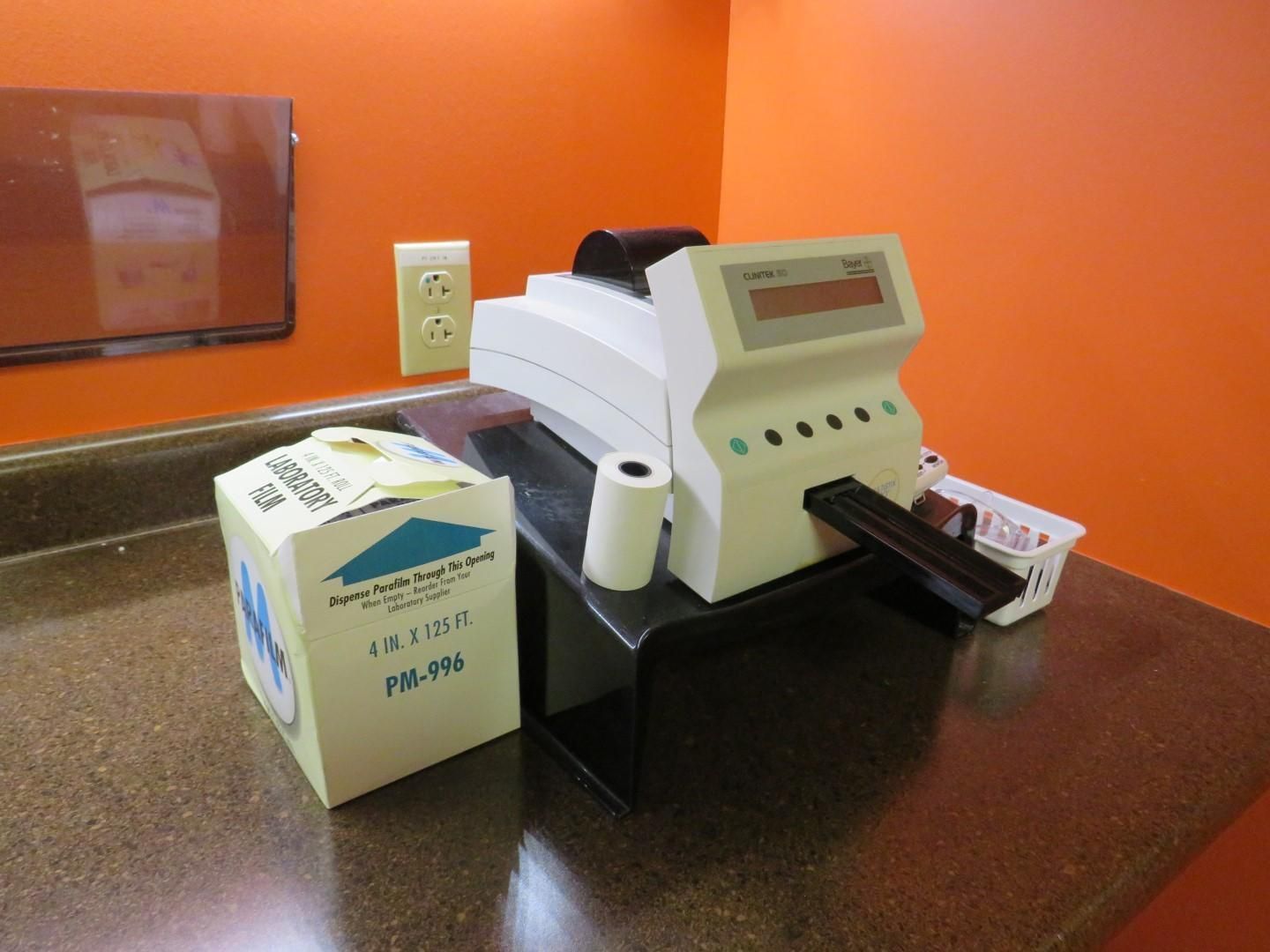 White medical machine on countertop with paper supply box, orange wall.