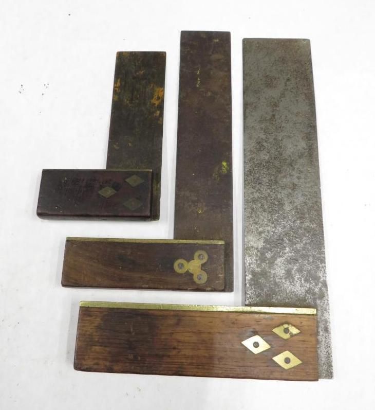 Collection of antique carpentry squares and blades on a white surface.