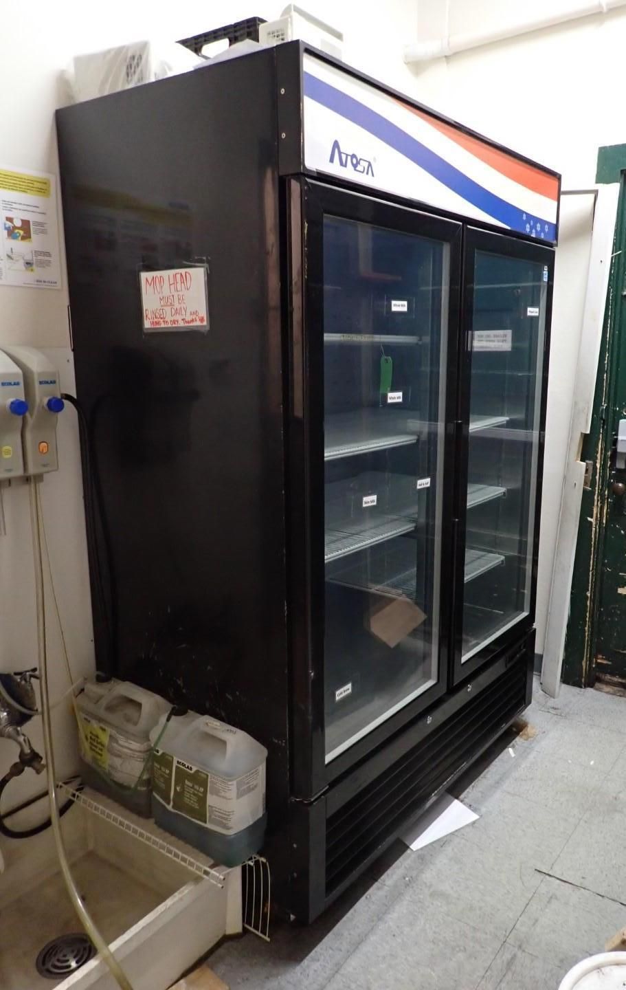 Black commercial refrigerator with glass doors, Pepsi logo on top, next to a sink with cleaning supplies.