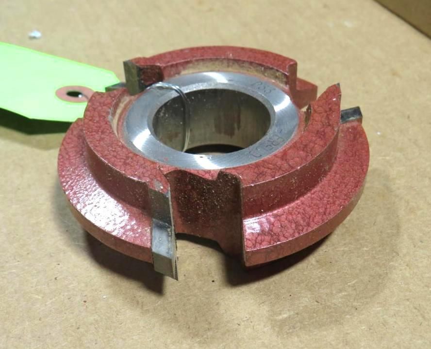 A red and silver router bit with a central cylindrical opening and cutting edges.