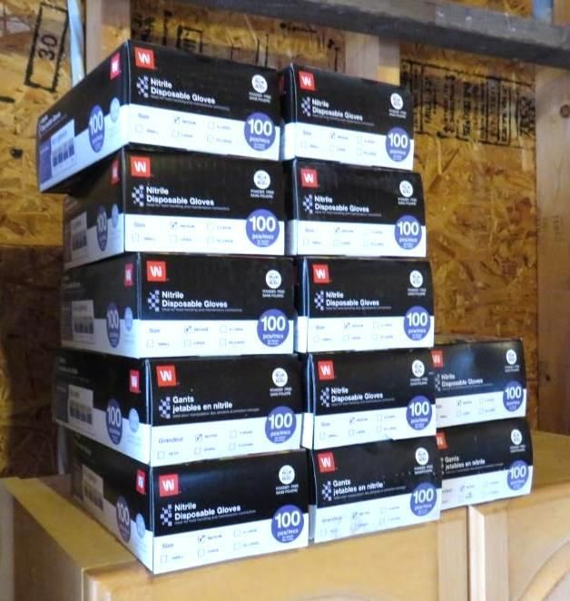 Boxes of white disposable gloves stacked on a wooden surface.