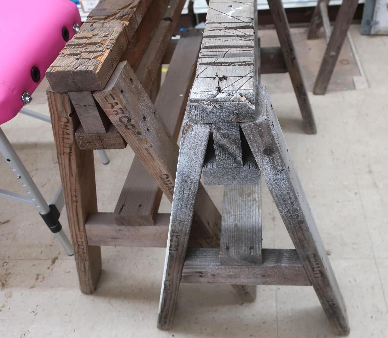 Two wooden sawhorses, one brown, one gray, on a light-colored floor.