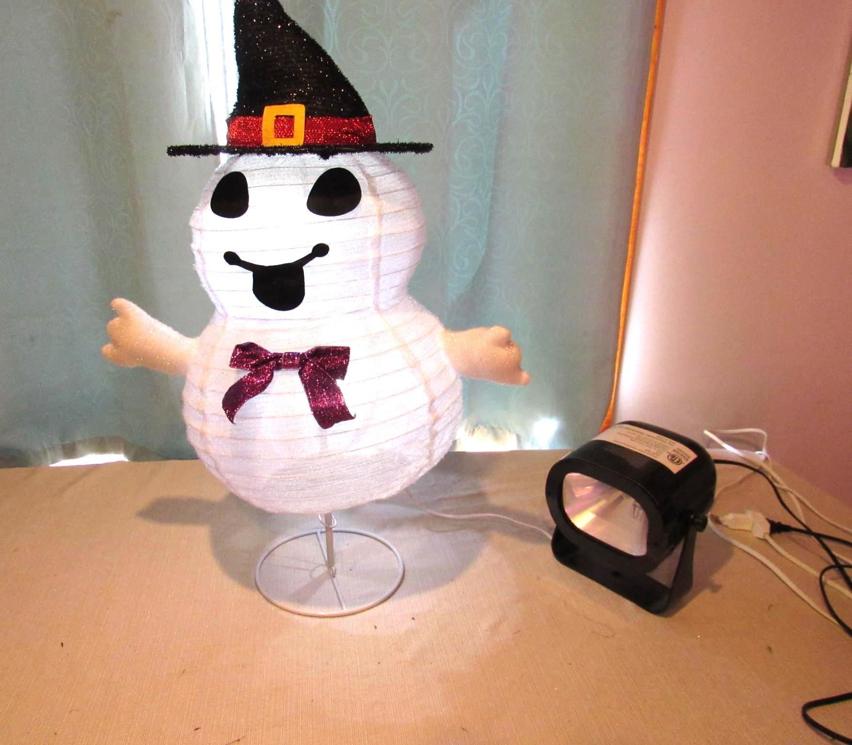 A white, snowman-shaped Halloween decoration wearing a witch hat and bow tie, with a spotlight next to it.