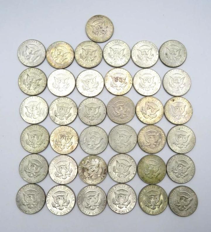 Silver Kennedy half dollar coins arranged in rows and columns on a white surface.