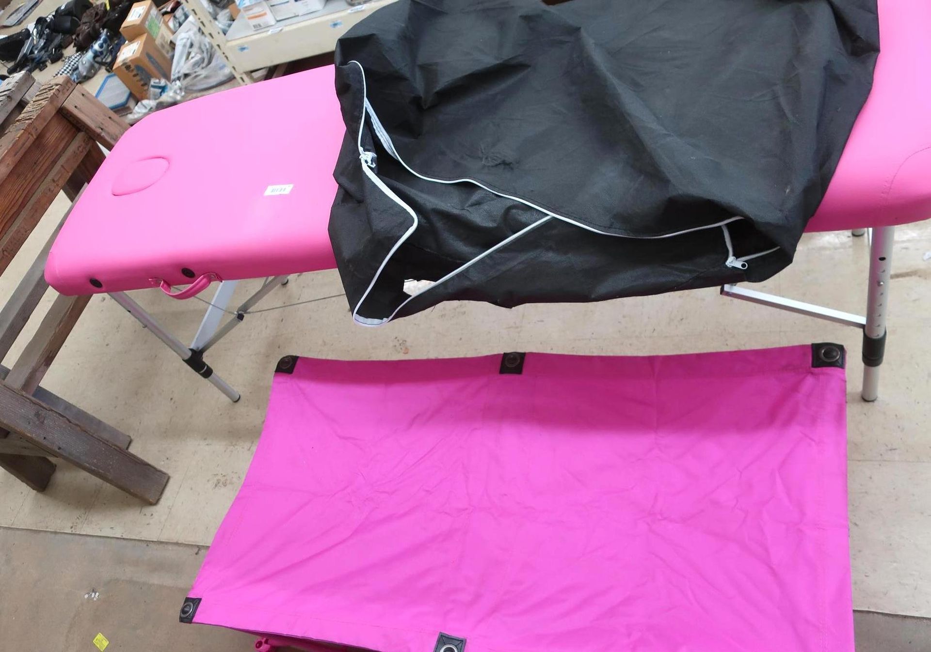 Pink massage table with black bag on top; pink foldable mat in front.