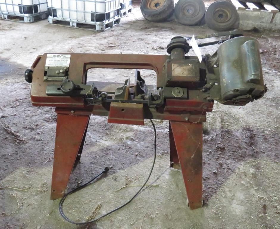 Red metal band saw on a stand, with a power cord, in a workshop setting.