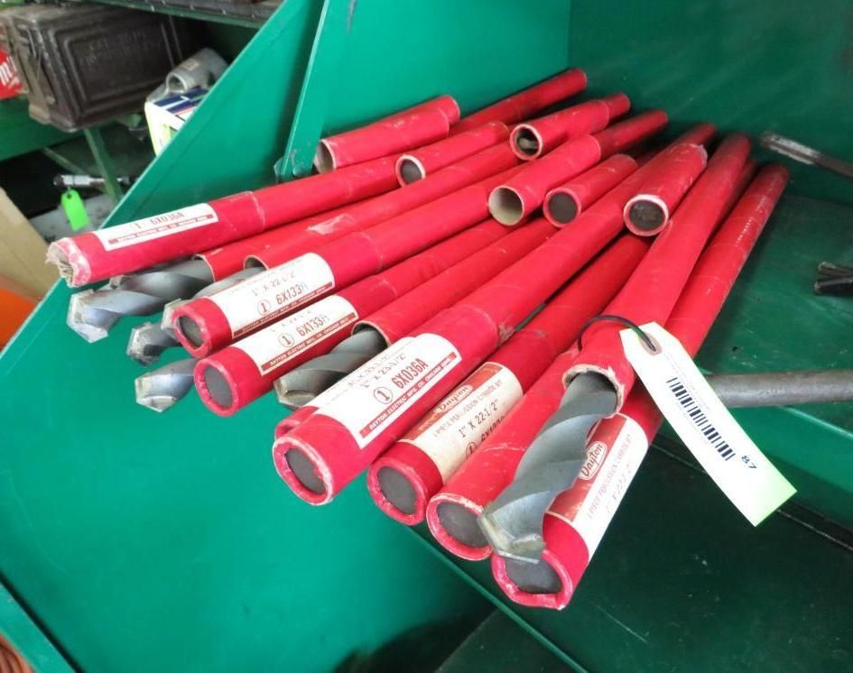 A pile of drill bits in red paper tubes, lying on a green surface.