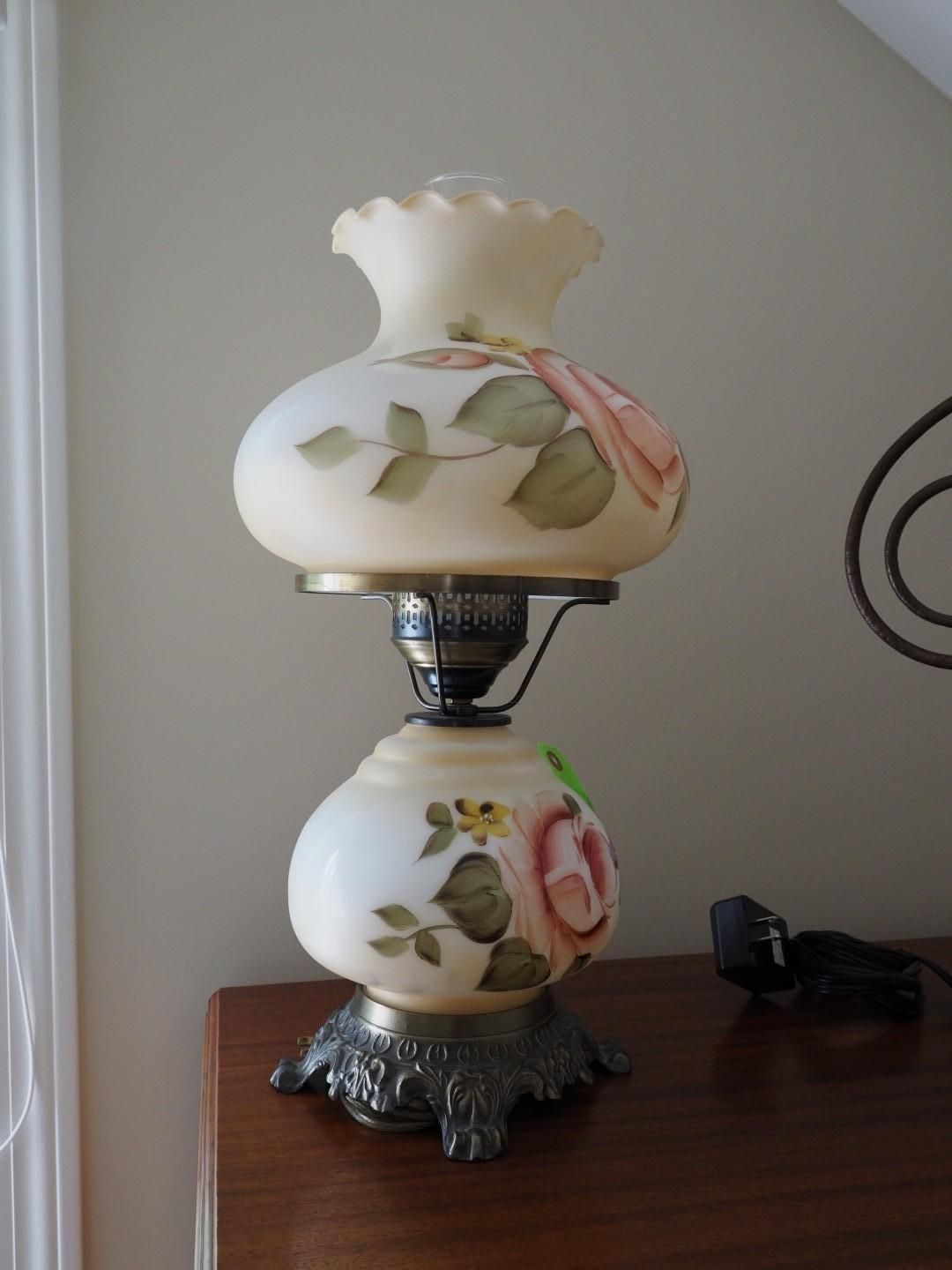 A vintage-style lamp with hand-painted roses on an ivory-colored glass globe and shade, set on a dark wooden surface.