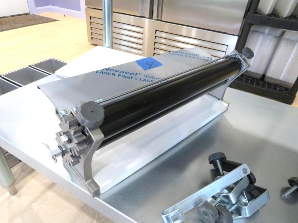 Commercial pasta machine on a stainless steel table, near other kitchen appliances.
