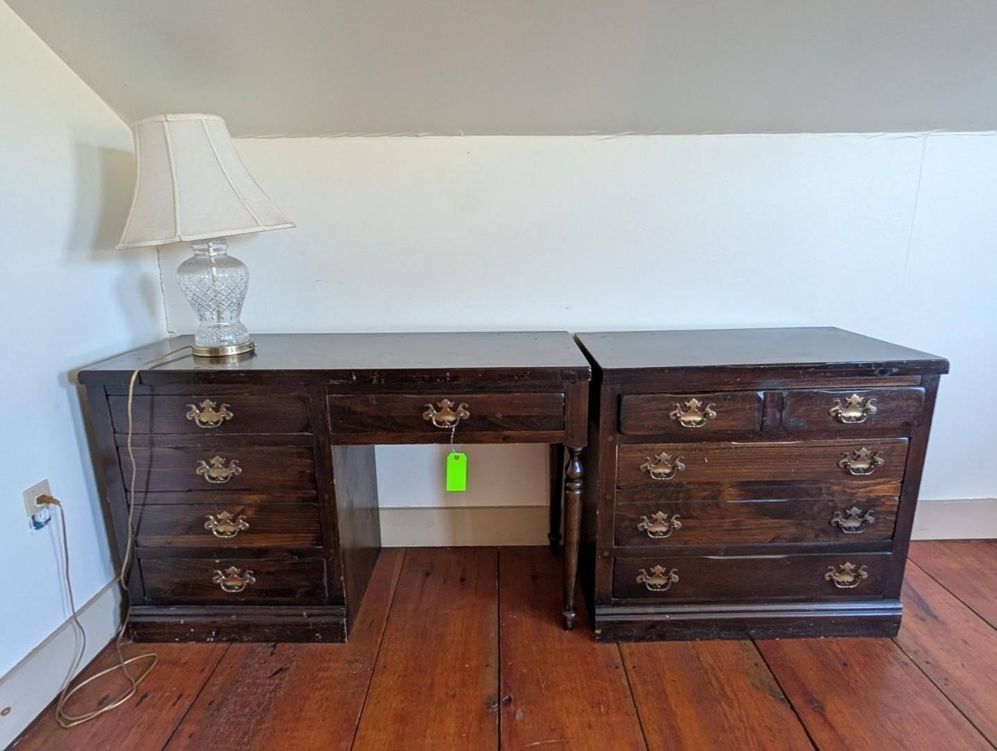 Dark wood double desk with drawers, centered under a white wall, with a lamp on the left side.