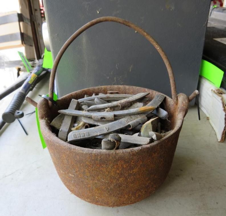 Cast iron pot filled with chisels and other metal tools, with a metal handle.
