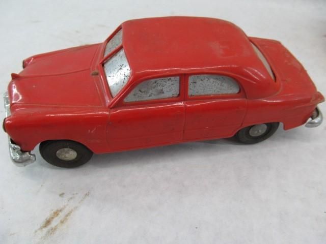 Vintage red toy car with silver bumpers and windows, on a light-colored surface.
