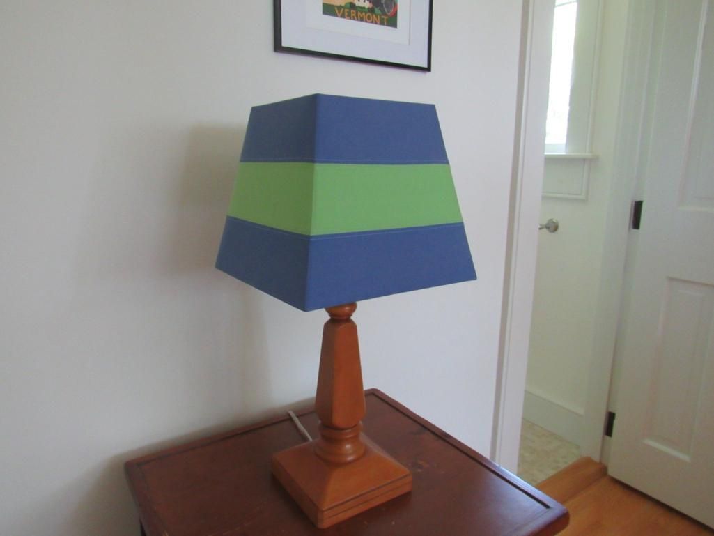 Wooden lamp with blue and green striped shade on a brown table in a room.