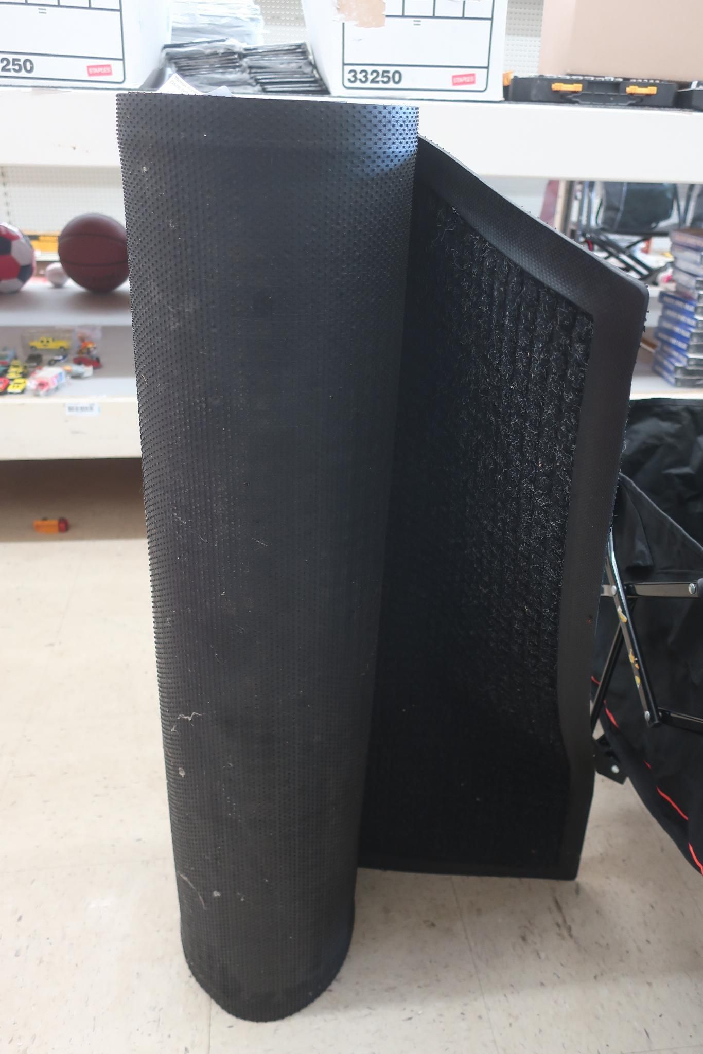 Black, cylindrical object with a textured surface, next to a black rectangular panel. Inside a store.