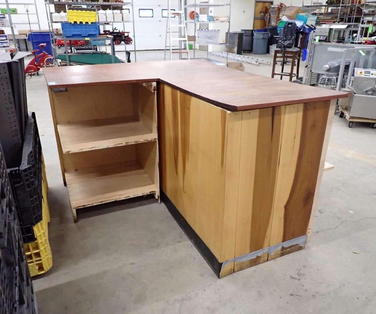 L-shaped wooden retail counter with shelves, light and dark wood tones, in a warehouse setting.