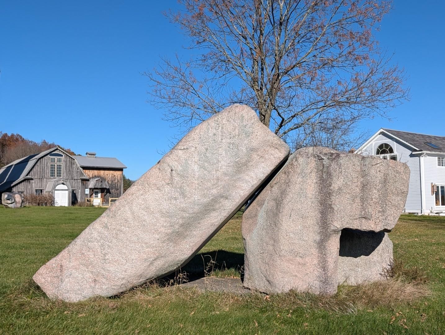 Large abstract stone sculpture in a grassy yard under a clear blue sky