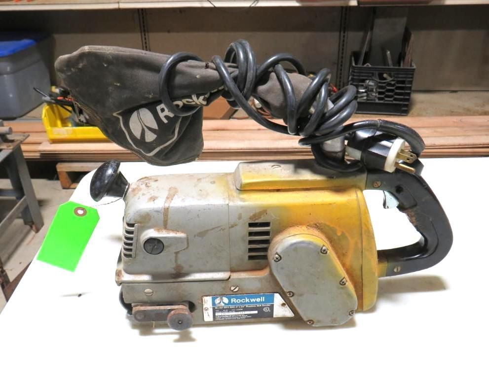 Belt sander with yellow and gray housing, black handle and cord, attached dust bag, and green tag.