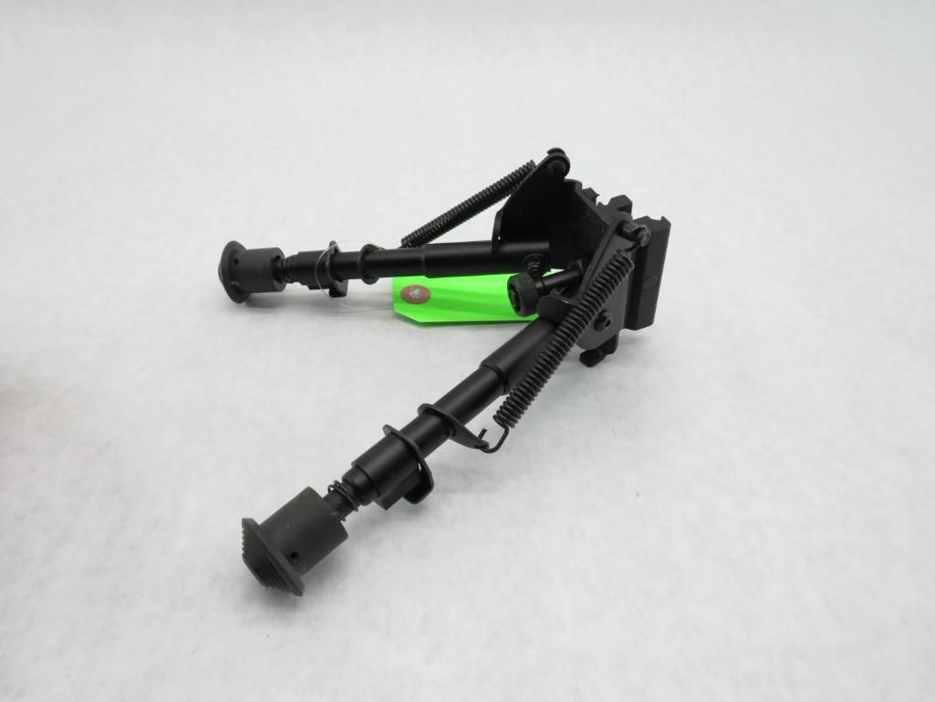 Black bipod, a two-legged stand for a rifle, with green tag attached.