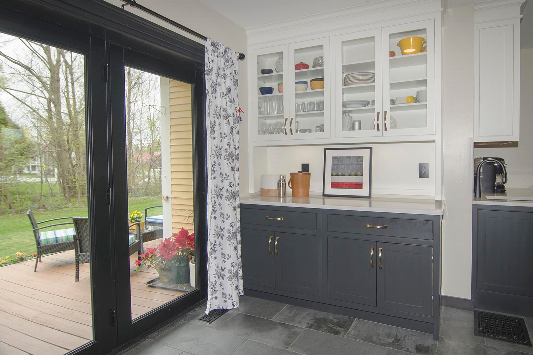 Kitchen with glass-front cabinets above dark grey cabinets. Sliding glass door leads to a deck.
