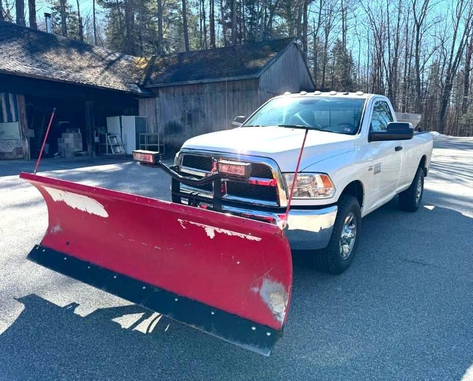 White pickup truck with a red snowplow parked in front of a wooden building.