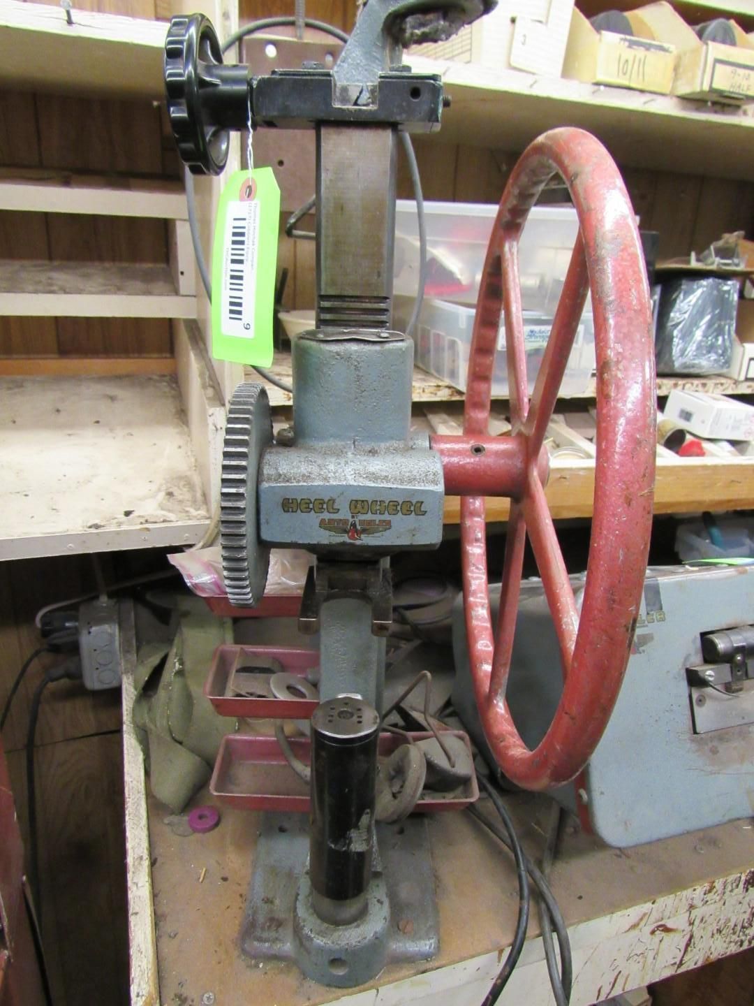 An industrial press machine with a large red wheel and gears, standing on a workbench.