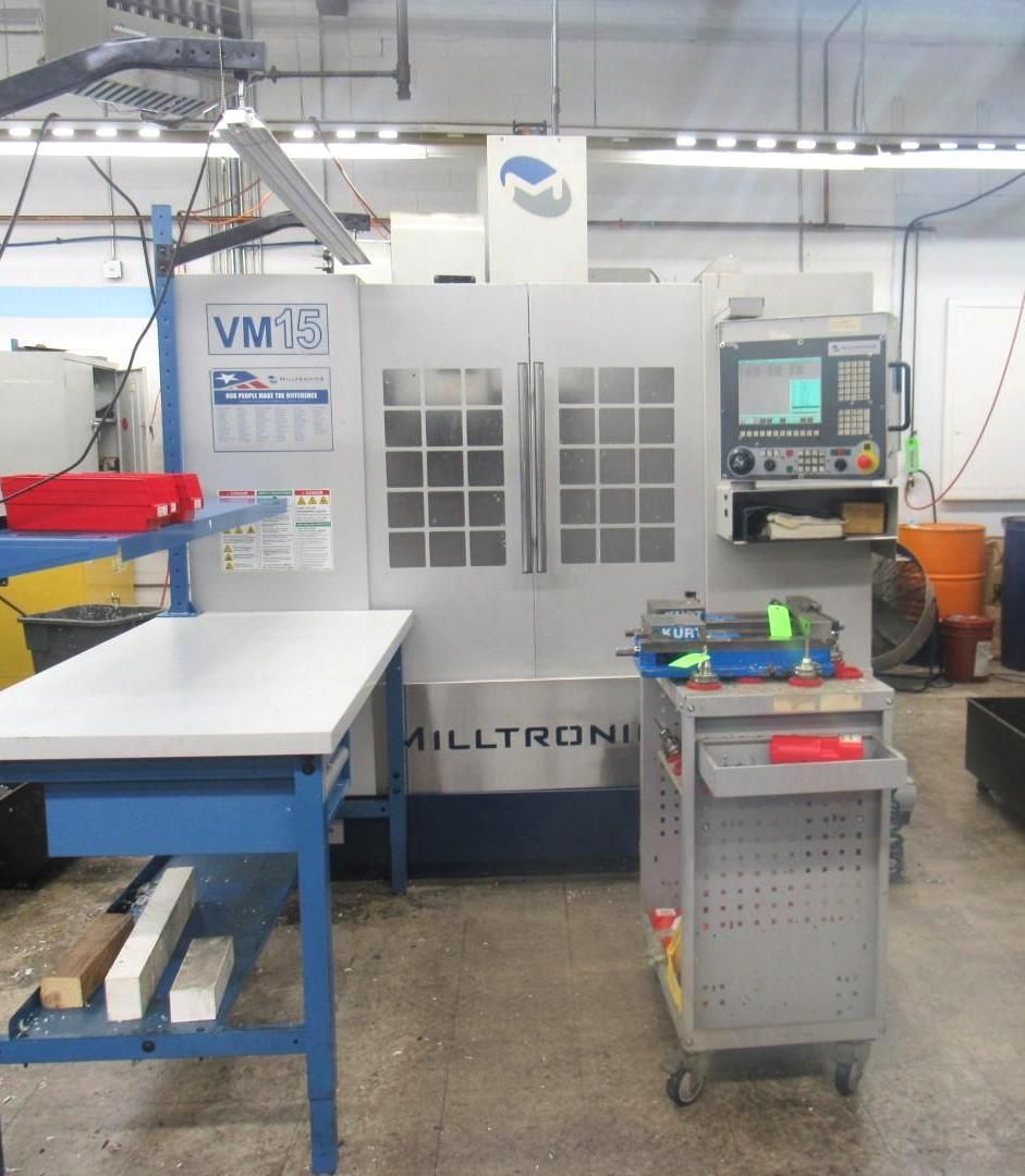 CNC milling machine in a workshop setting. The machine is gray, with a control panel.