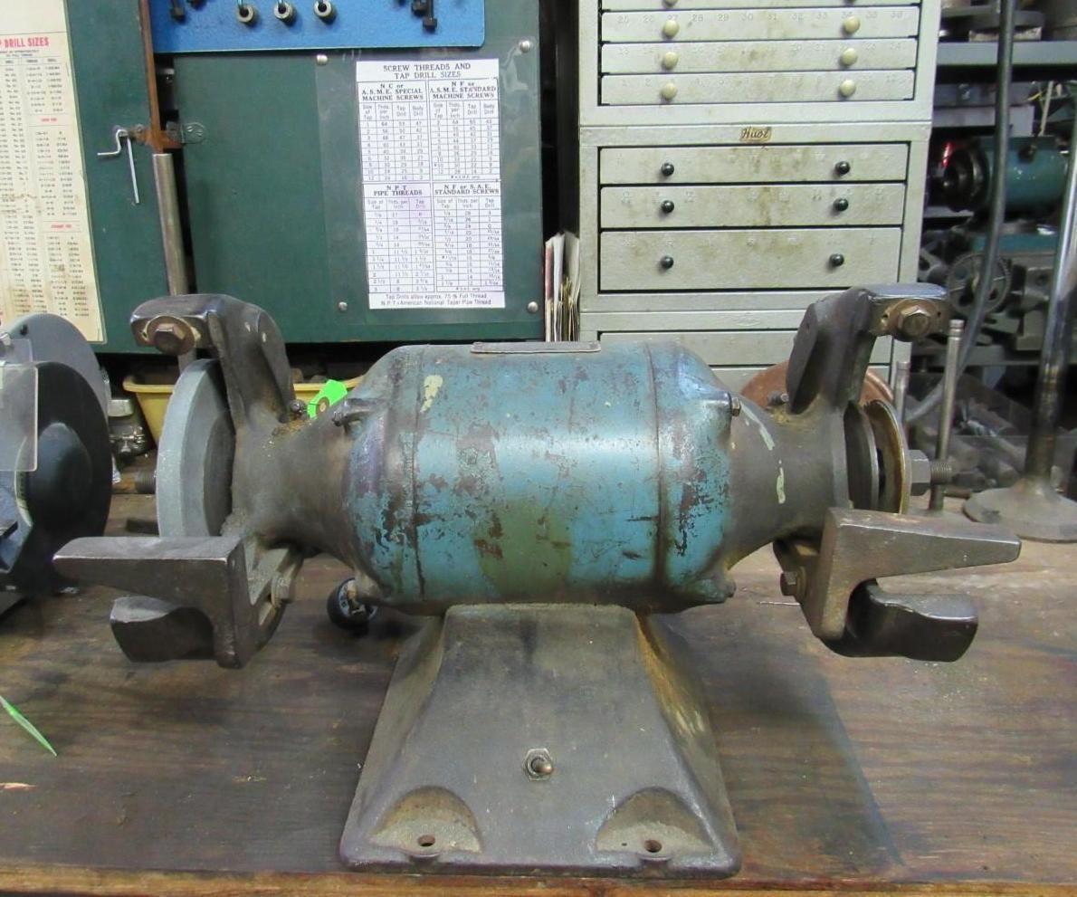 Bench grinder in a workshop. Teal and gray metal, with grinding wheels on either side.