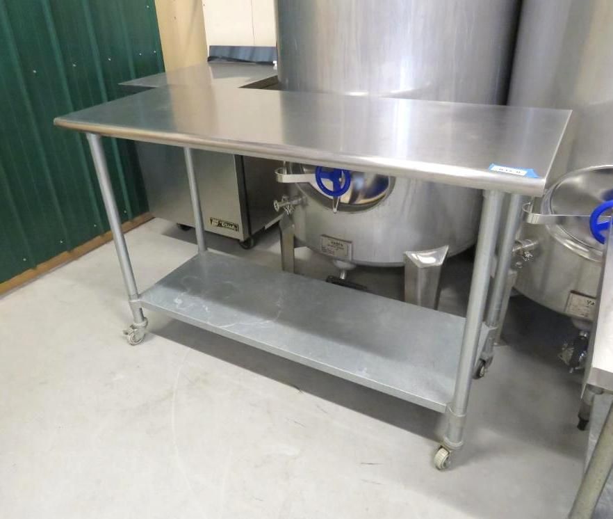Stainless steel work table with a shelf and casters in a commercial kitchen setting.