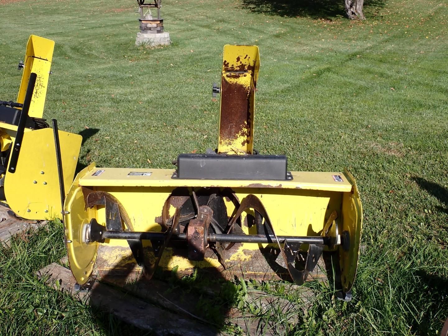 Yellow snowblower on a grassy lawn, with augers and a vertical chute.