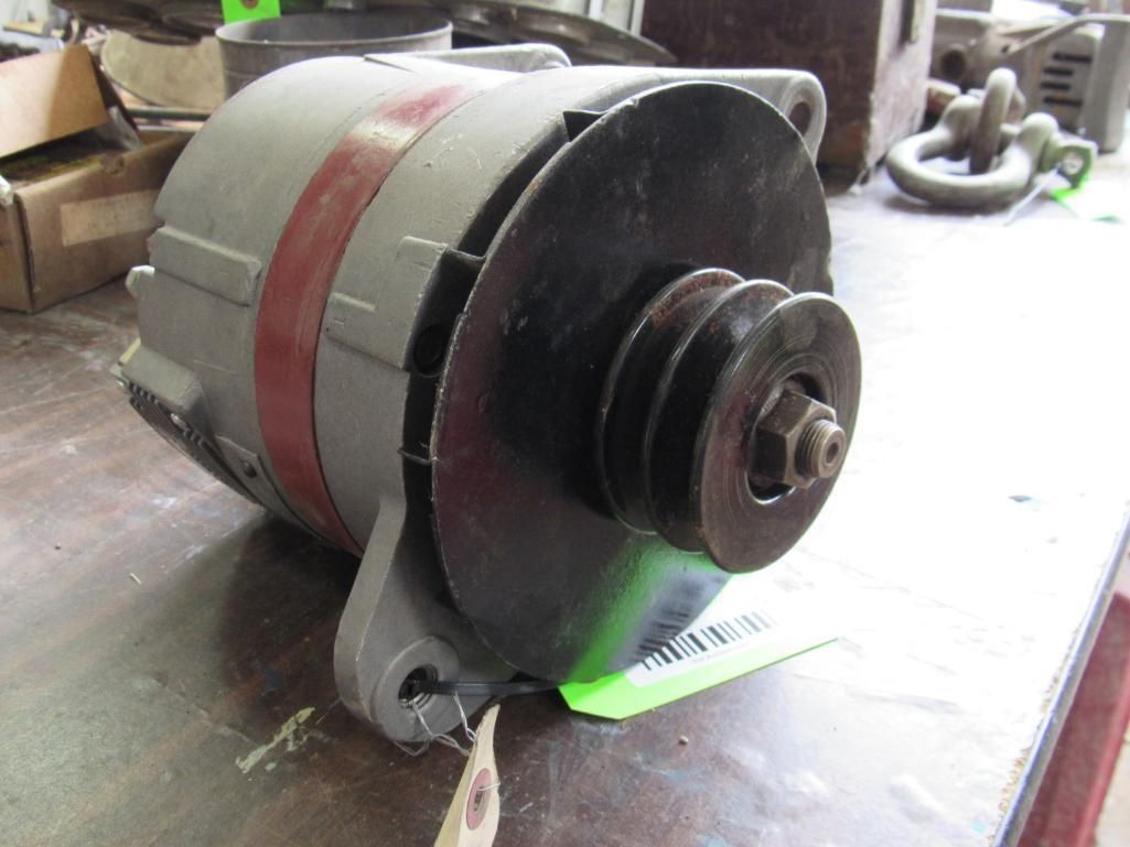 Gray alternator with a black pulley. Red stripe around the middle. Sitting on a wooden surface.