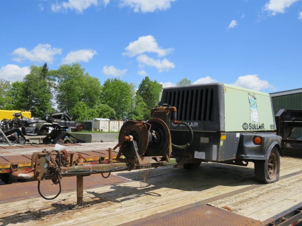 Mobile air compressor on a trailer in an outdoor yard, green and black.