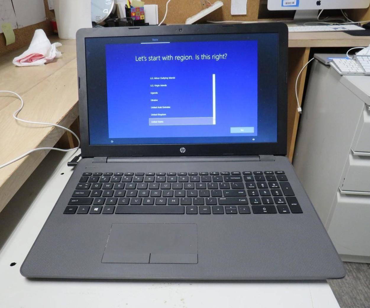 Laptop displaying a blue Windows setup screen. The HP laptop sits on a desk with a keyboard nearby.