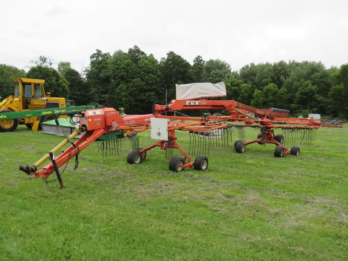 Orange agricultural hay rake in a grassy field.
