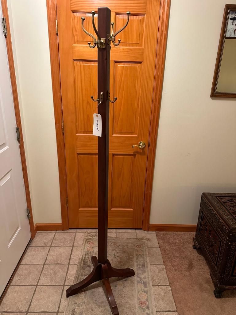 Dark wood coat rack with brass hooks stands in front of a wooden door.
