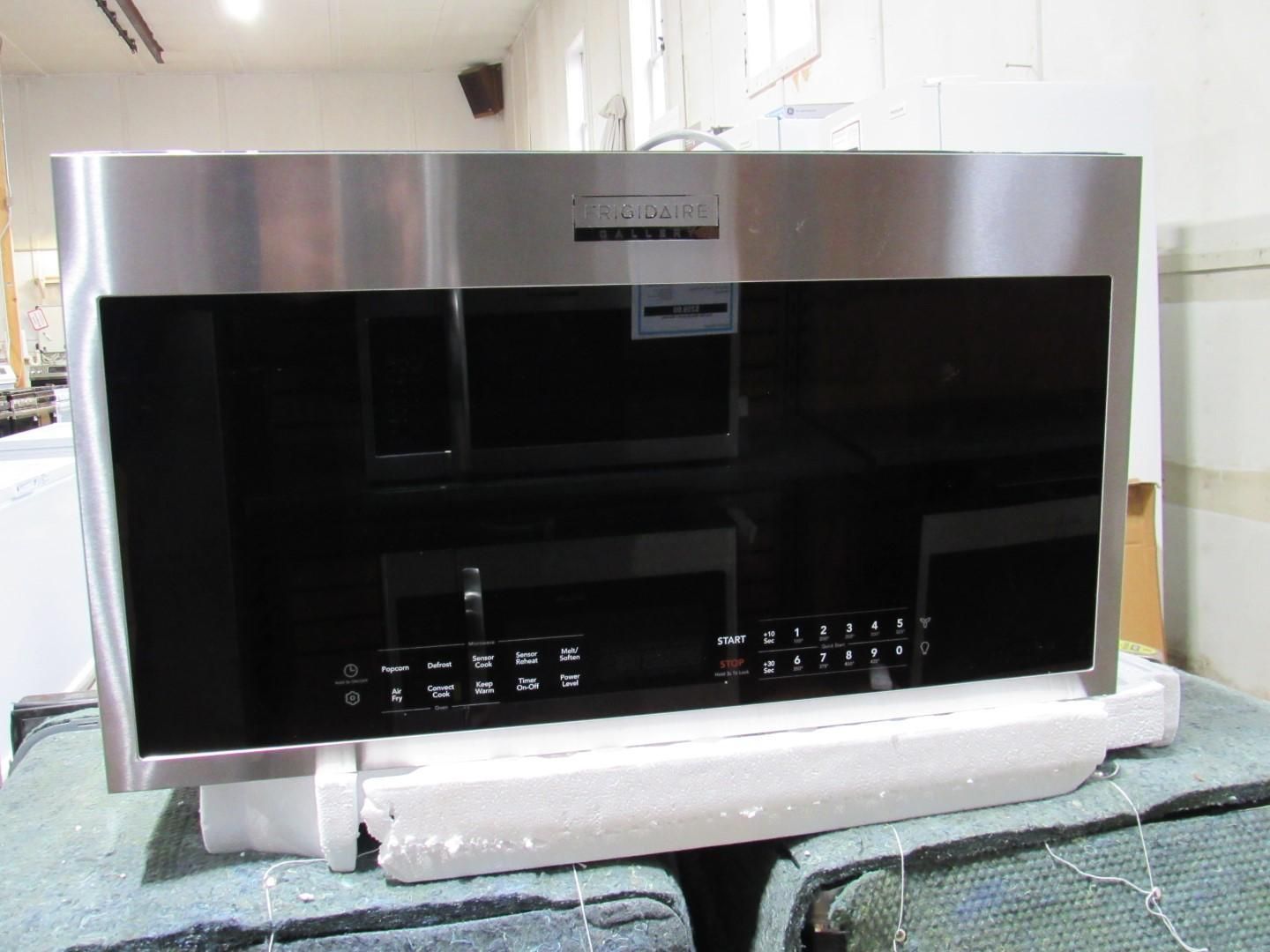 Stainless steel built-in microwave oven with black glass front panel and control buttons on a white foam base.