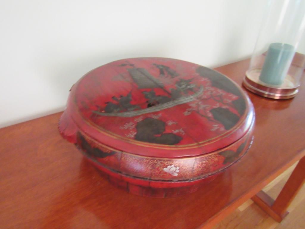 Red and black circular box on a wooden table, possibly antique.