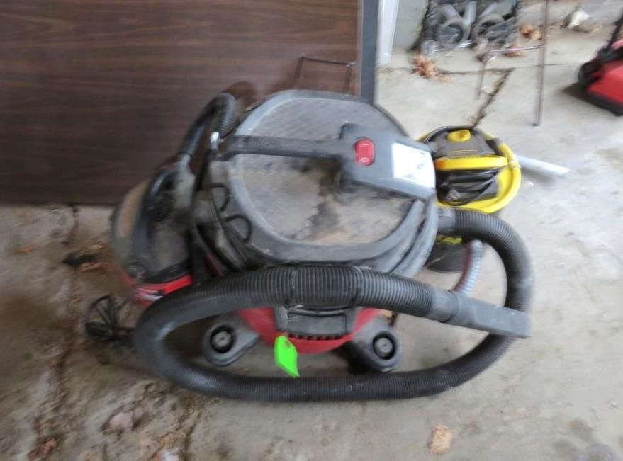 A dirty wet/dry vacuum cleaner with a black hose and handle rests on concrete.