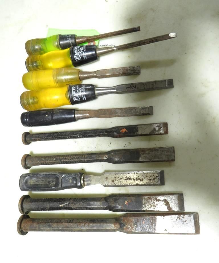 Nine chisels with various handle colors and shapes, resting on a surface.