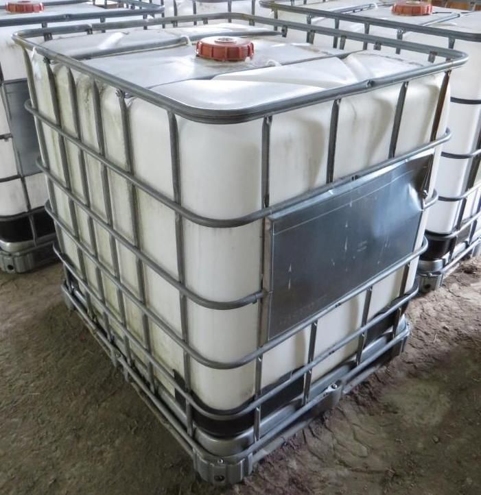 White plastic IBC tote in a metal cage with a red cap, outside.