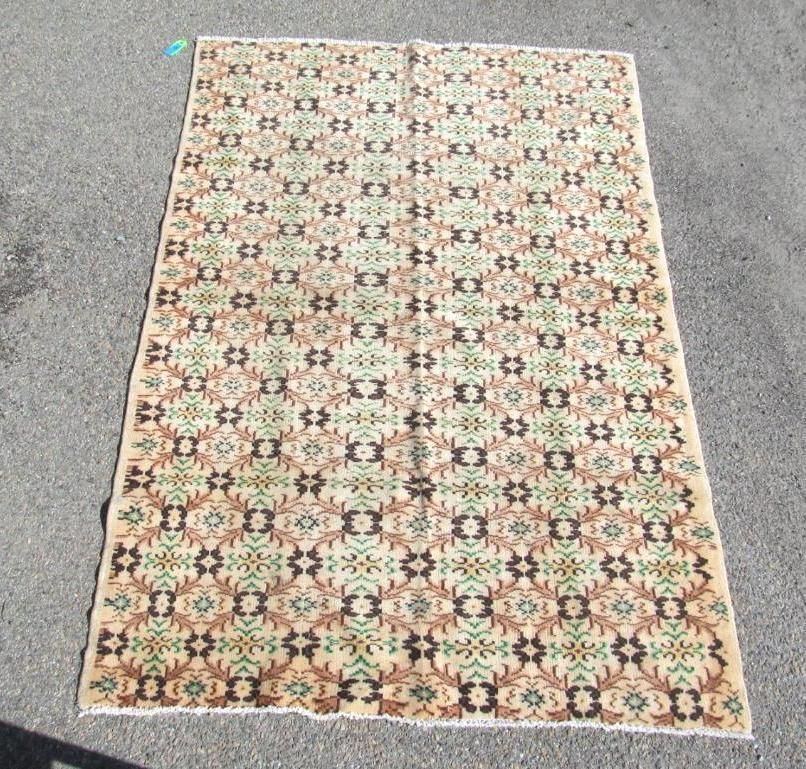Tan and brown patterned rug on a gray surface, with green and black accents.