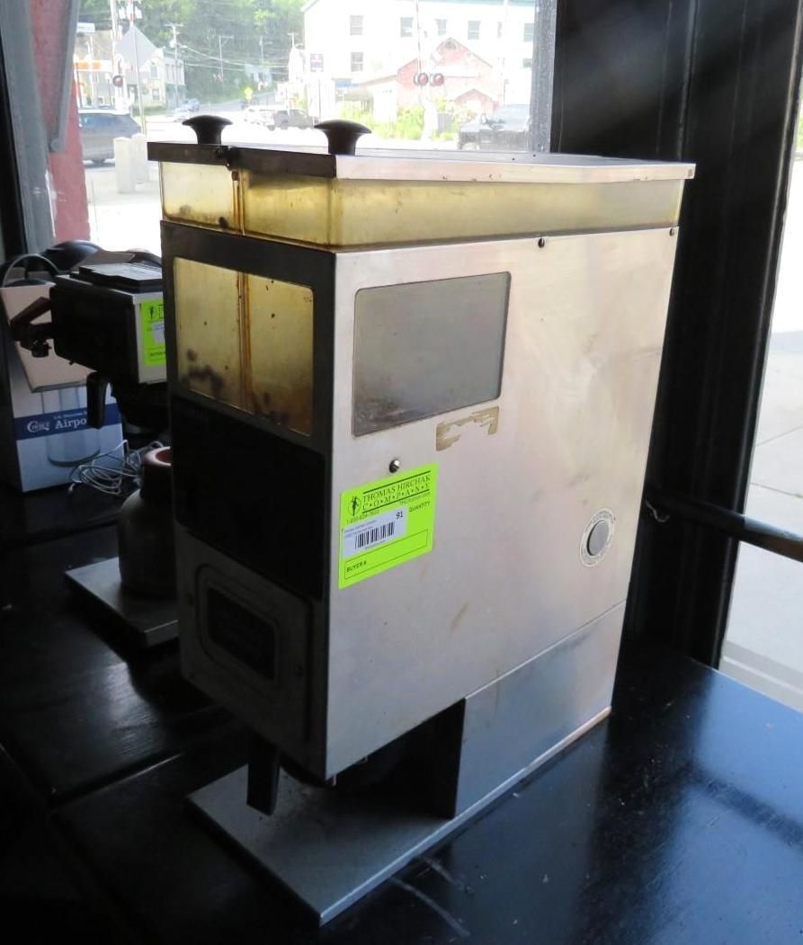 Stainless steel commercial coffee grinder with hopper, inside a building.